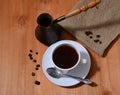 Poured black coffee into a white cup near the turk and coffee grains on burlap and wooden table