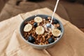 Pouring, adding milk to homemade granola in a plate with nuts, honey, blueberries and banana, served on napkin