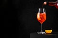 Pouring Aperol Spritz Cocktail in wine glass with ice and orange slice on dark background. Long fizzy drink Royalty Free Stock Photo