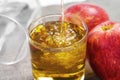 Pouring apple cider into a glass on a table with juicy red apples