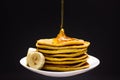 Pouring banana honey pancakes with maple syrup on a white plate. Dark background Royalty Free Stock Photo