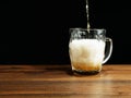 Pouring beer into big glass jar on a brown wooden table. Alcohol consumption. Dark background Royalty Free Stock Photo