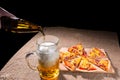 Pouring Beer into Glass next to Pizza Slices Royalty Free Stock Photo