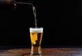 Pouring beer in a glass on a wooden table, dark background Royalty Free Stock Photo