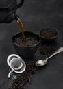 Pouring black tea from teapot to cup with strainer infuser and loose tea on black with silver spoon Royalty Free Stock Photo