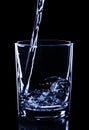 Pouring blue water on glass isolated on black, close up, concept Royalty Free Stock Photo