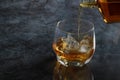 Pouring brandy alcohol drinks into the glass of brandy with ice cubes and reflective on black counter bar background Royalty Free Stock Photo