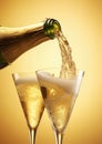 Pouring champagne from bottle in to glasses with splash on golden background