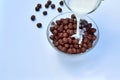 Pouring chocolate cereal balls with milk into a glass bowl on a light background. close-up Royalty Free Stock Photo