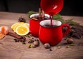 Pouring of Christmas mulled red wine with spices, cinnamon stick, apples and citrus fruits orange, lemon into a two red cups on a Royalty Free Stock Photo