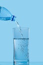 Pouring clean drinking water from blue plastic bottle into glass on blue background Royalty Free Stock Photo