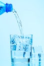 Pouring clean drinking water from blue plastic bottle into glass on blue background Royalty Free Stock Photo