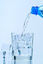 Pouring clean drinking water from blue plastic bottle into glass on blue background Royalty Free Stock Photo