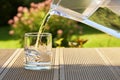 Pouring clear filtered water from a water filtration jug into a glass in green summer garden in a sunny summer day Royalty Free Stock Photo