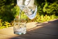 Pouring clear filtered water from a water filtration jug into a glass in green summer garden in a sunny summer day Royalty Free Stock Photo