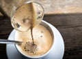 pouring coffee into cappuccino cup on the retro wooden table background.