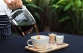 Pouring coffee into a cup on a wooden tray. placed on a table covered with a black tablecloth. Royalty Free Stock Photo