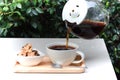 Pouring coffee from a pot to cup, cookies beside coffee cup on wood tray, white table. Royalty Free Stock Photo