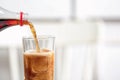 Pouring cola from bottle into glass on blurred background, closeup. Royalty Free Stock Photo