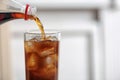 Pouring cola from bottle into glass on blurred background. Space for text Royalty Free Stock Photo