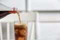 Pouring cola from bottle into glass on blurred background, closeup. Royalty Free Stock Photo