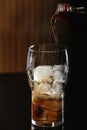 Pouring cola from bottle into glass with ice cubes on table Royalty Free Stock Photo