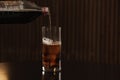 Pouring cola from bottle into glass with ice cubes on table against blurred background. Royalty Free Stock Photo