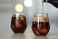 Pouring cola from bottle into glass with ice cubes on table against blurred background. Royalty Free Stock Photo