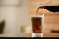 Pouring cola from bottle into glass with ice cubes on table against blurred background Royalty Free Stock Photo