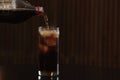 Pouring cola from bottle into glass with ice cubes on table against blurred background Royalty Free Stock Photo