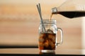 Pouring cola from bottle into mason jar with ice cubes on table against blurred background. Royalty Free Stock Photo