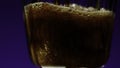 Pouring Cola with bubbles into the glass, close up. Stock clip. Coke soda in transparent glass on a colorful lighted Royalty Free Stock Photo