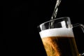 Pouring cold tasty beer into glass mug on black background, closeup. Space for text Royalty Free Stock Photo
