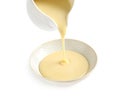 Pouring condensed milk from jug into bowl on white. Dairy product