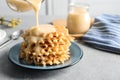 Pouring condensed milk from jug onto waffles on grey, space for text. Dairy product Royalty Free Stock Photo