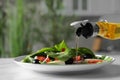 Pouring cooking oil onto plate with salad on white table, closeup Royalty Free Stock Photo