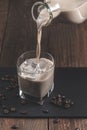 Pouring  Cream coffee liqueur in a glass with ice, surrounded by coffee beans on a dark wooden background Royalty Free Stock Photo