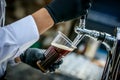 Pouring dark beer to plastic glass from beer tap. Royalty Free Stock Photo
