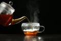 Pouring delicious hot tea into glass cup on table against dark