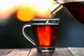 Pouring delicious tea into glass cup on wooden table against blurred background, closeup Royalty Free Stock Photo