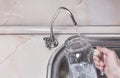 Pouring drinkable water into glass jug from water filter. Closeup of sink and faucet. Filtered water i Royalty Free Stock Photo