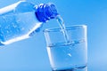 Pouring drinking water from bottle into glass on blue background Royalty Free Stock Photo