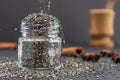 Pouring dry chia seeds in glass jar with unfocused objects on background. Copy space. Royalty Free Stock Photo