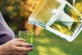 Pouring filtered water from a water filtration jug into a glass which female hand holding in summer garden Royalty Free Stock Photo