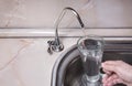 Pouring filtered water into glass from water filter. Close up of sink and faucet. Drinkable water in kitchen Royalty Free Stock Photo