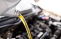 Pouring fresh automotive engine oil lubricating oil, yellow liquid oil into a motor car with a blurred engine background. Change