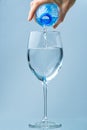 Pouring clean drinking water from blue plastic bottle into glass on blue background Royalty Free Stock Photo