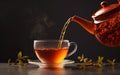 Pouring fresh and hot Rooibos tea from the teapot to a glass cup, dark background