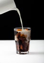 Pouring fresh milk into glass of black coffee with ice cubes on white board and black backdrop Royalty Free Stock Photo