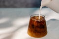 Pouring Fresh Milk into a Glass of Ice Coffee. Making Cold Drink in a hot Summer Day Royalty Free Stock Photo